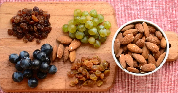 Various raisins, vine berries and almonds on chopping board — Stock Photo, Image