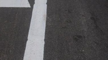 Beyaz bisiklet sembolü asfalt bisiklet yoluna yön işaretleri ile boyanmış. Koyu asfalt yüzeyde beyaz bisiklet sembolü ve şerit işaretlerinin yakın görüntüsü, kendini adamış bir bisiklet yolunu gösterir