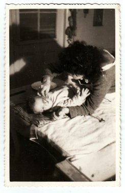 Vintage photo shows mother feeds her baby girl, circa 1940.