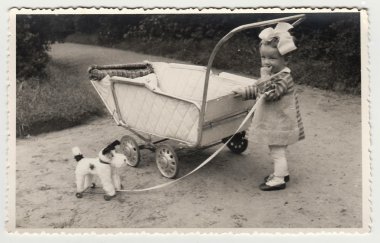 Vintage photo shows a small girl with dog toy and pram (baby carriage), circa 1942.