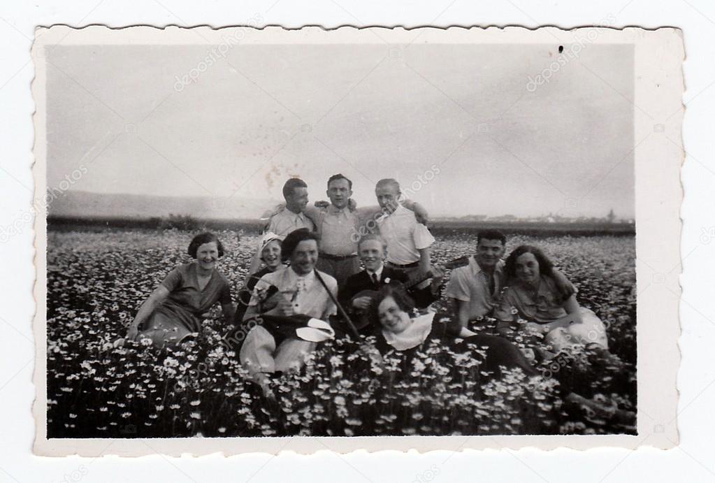 Vintage photo shows people sit on meadow, circa 1935.