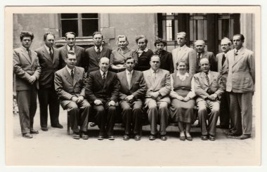 Vintage photo shows group of people in front of building, circa 1960s.