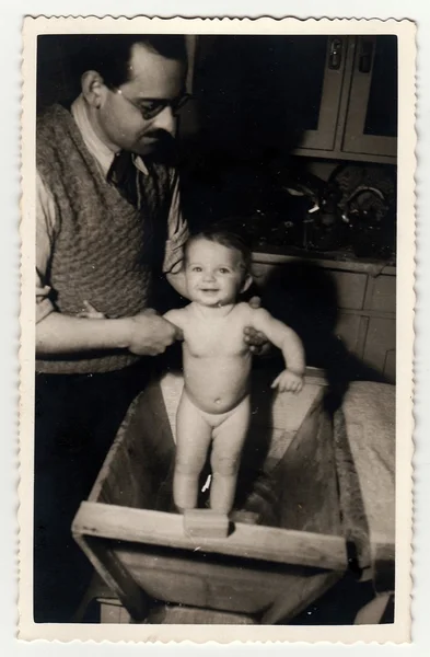 A vintage photo shows father with baby girl. He takes a bath her, circa 1940. — ストック写真