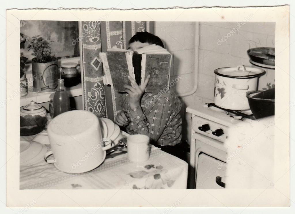 Vintage photo shows a small boy covers up his face by book.