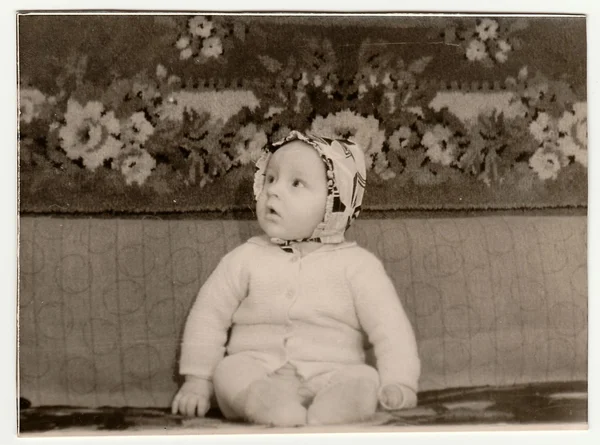 Vintage portrait shows toddler sits on sofa.  Black & white antique photo.