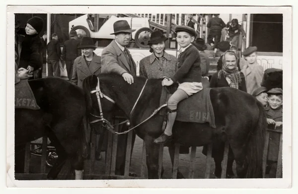 Foto vintage muestra a la familia en el parque de atracciones. Un niño pequeño se sienta a caballo . — Foto de Stock