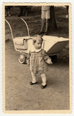 Bir vintage fotoğraf küçük yürümeye başlayan kız ve bebek arabası (bebek arabası) gösterir. Toddler sevimli yüz gösterir.