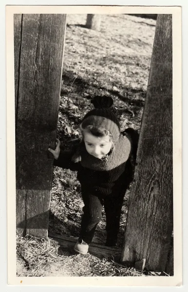 Uma foto vintage mostra menina pequena atravessa o buraco na cerca de madeira . — Fotografia de Stock