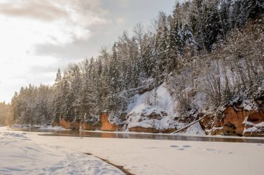 Kışın Letonya 'daki Gauja Milli Parkı' nda Gauja nehri kıyısındaki kayalık ve mağara.