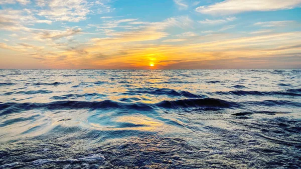 A restless sea with orange sunset skies and sun through clouds over. Meditation ocean and sky background. Quiet sea landscape. Horizon above water. Warm summer evening