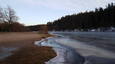 Kış manzarası. Kışın kumsalda donmuş nehir. Mavi gökyüzü ve yapraksız ağaçlar