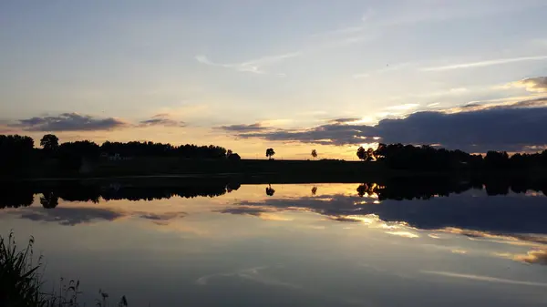 Misty lake - calm water surface of the lake reflects sky with yellow and blue clouds after sunset. Blur filter, space for copy.