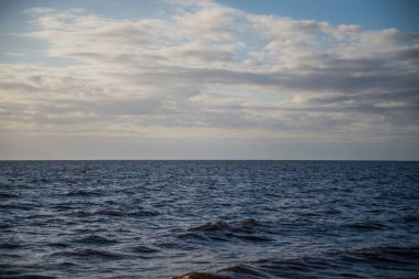 Mavi dalgalı su ve küçük beyaz kümülüs bulutlu mavi gökyüzü ile güzel deniz manzarası. Gün batımından önceki akşam. Güzel deniz manzarası
