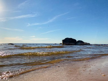 Sakin dalgalarla deniz manzarası ve deniz kıyısında mavi deniz suyuyla yıkanmış dev bir kaya. Mavi gökyüzü ve kuş siluetleriyle dolu bereketli bir yaz günü.