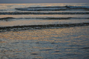 close-up of sea water waves with bubbles. Blue sea water at sunset.