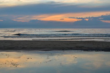 Kırmızı ve turuncu renkli gökyüzü ve kıyıda kırma dalgalar deniz sahilde dramatik günbatımı