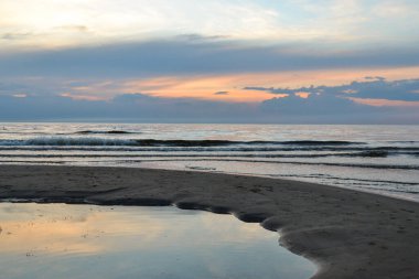 Kırmızı ve turuncu renkli gökyüzü ve kıyıda kırma dalgalar deniz sahilde dramatik günbatımı