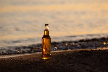 Gün batımında sahilde bir şişe bira.