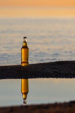 Gün batımında sahilde bir şişe bira.