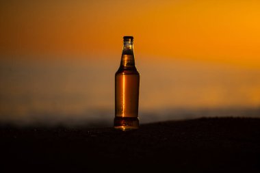 Gün batımında altın kumların üzerinde duran buz gibi bir bira / soda şişesi. Yaz akşamı.