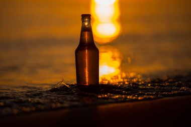 Gün batımında sahilde bir şişe light bira. Dalgalı deniz kıyısı. Bokeh arkaplanı.