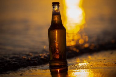 Gün batımı deniz suyunda bira şişesi ve arka planda Bokeh.