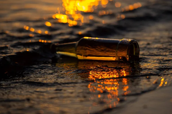 将啤酒瓶倒入夕阳西下的海水中 背景为Bokeh 水中为Glare — 图库照片