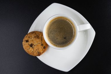 Üst Manzara. Beyaz kahve kupası, bisküvi ve siyah arka planda kahve.