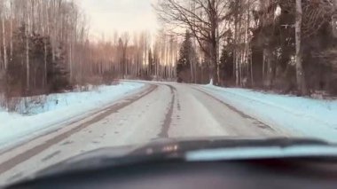 Gün batımında keskin kıvrımlı ve buzla kaplı tehlikeli bir orman yolunda ilerleyen bir arabanın ön camından bakın. Donmuş asfalt ile kaygan kış yolu koşulları.