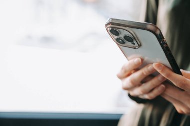 Üç kameralı modern akıllı telefonu tutan ve kullanan bir kadının yakın çekimi. Kopya alanı ile en düşük, yumuşak ışık bileşimi, teknoloji, iletişim, iş ve dijital yaşam tarzı kavramları için ideal.