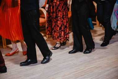 Kapalı bir kutlamada resmi ayakkabılar içinde dans eden zarif giyimli yetişkinlerin yakın çekimi. Kırpılmış bacak ve ayakkabı görüntüsü hareket, tarz ve şenlik atmosferi yaşam tarzı, olaylar ve sosyal kavramlar için idealdir..