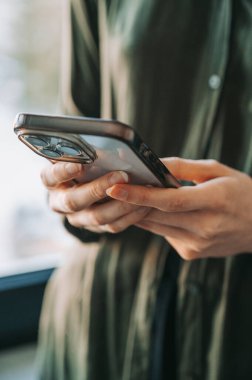 Kapalı mekanda akıllı telefon kullanan bir kadının yakın çekimi. Doğal ışık, sığ alan derinliği ve iş, teknoloji veya sosyal medya temaları için kopyalama alanı ile modern yaşam tarzı ve dijital iletişim kavramı.