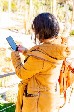 Botanik bahçesinde fotoğraf çeken kahverengi ceketli esmer kız.