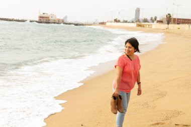 Plajda çıplak ayaklı bir kadın elinde botlarıyla Barselona 'da, moda anlayışı.