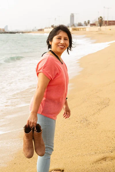 Plajda çıplak ayaklı bir kadın elinde botlarıyla Barselona 'da, moda anlayışı.