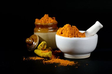 Havanda zerdeçal tozu, kabuklu ve kökleri siyah arkaplanda kil çömlek.