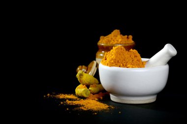 Havanda zerdeçal tozu, kabuklu ve kökleri siyah arkaplanda kil çömlek.