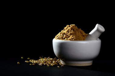 Kişniş tozu ve siyah zemin üzerinde harç ve tokmak olan tohumlar.