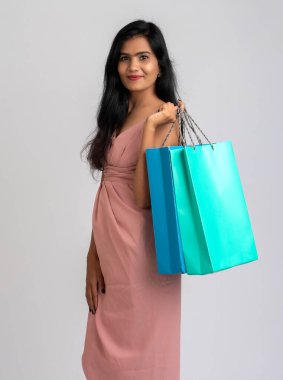 Gri bir arka planda alışveriş torbalarıyla poz veren güzel bir genç kız.