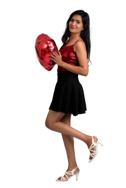 Gri arka planda kalp şeklinde bir balonla poz veren süslü elbiseli neşeli tatlı kız.