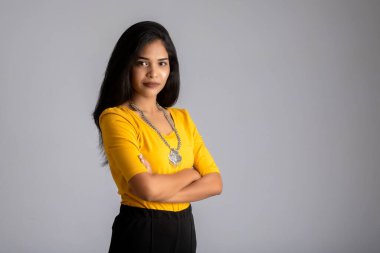 Gri arka planda elleri bağlı poz veren güzel, gülümseyen, duygusal bir genç kadının portresi..