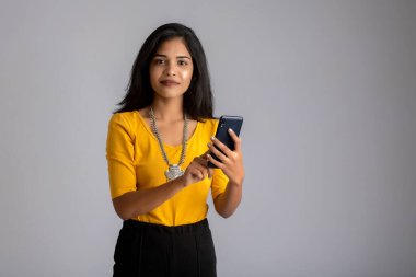 Gri arka planda cep telefonu ya da akıllı telefon kullanan genç kız