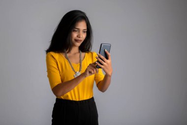 Gri arka planda cep telefonu ya da akıllı telefon kullanan genç kız