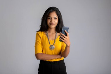 Gri arka planda cep telefonu ya da akıllı telefon kullanan genç kız