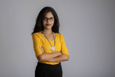 Gri arka planda elleri bağlı poz veren güzel, gülümseyen, duygusal bir genç kadının portresi..