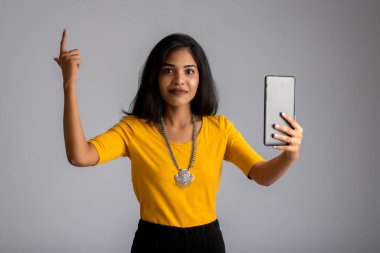 Gri arka planda cep telefonu ya da akıllı telefon kullanan genç kız