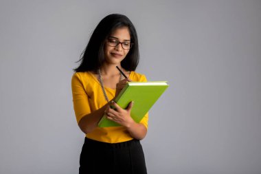 Gri arkaplanlı kitapla poz veren güzel genç kız.