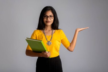 Gri arkaplanlı kitapla poz veren güzel genç kız.