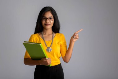 Gri arkaplanlı kitapla poz veren güzel genç kız.