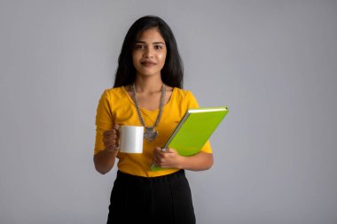 Gri arka planda bir fincan çay ya da kahve duran güzel genç bir kız.